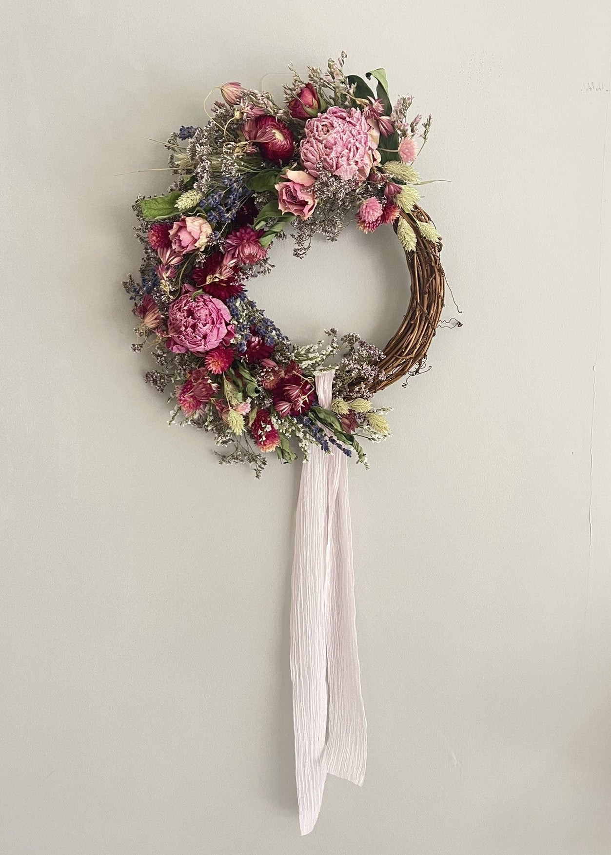 Floral wreath with pink flowers and a white ribbon on a light gray background