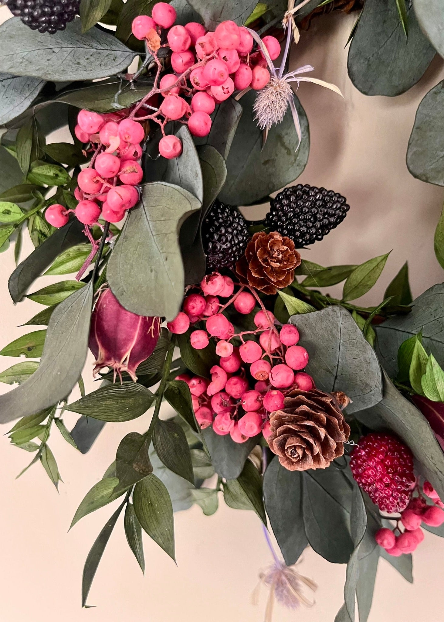 Decorative wreath with pink berries, green leaves, and other elements on a neutral background