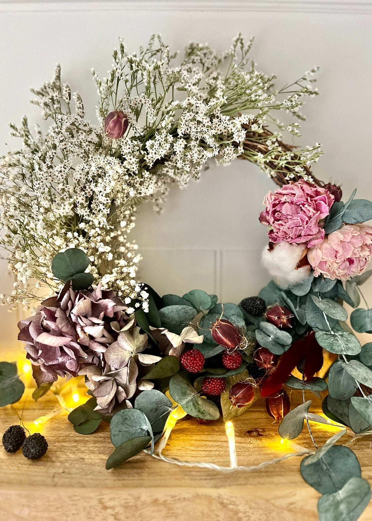 Decorative wreath with flowers and lights on a wooden surface