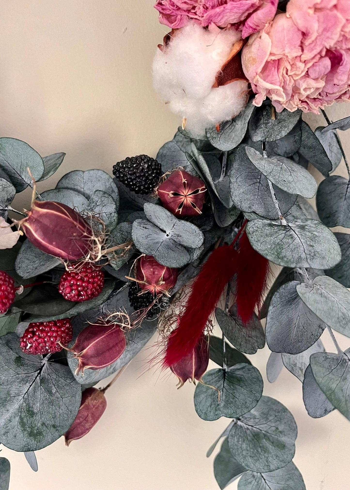 Decorative wreath with pink flowers, cotton, and eucalyptus leaves on a neutral background