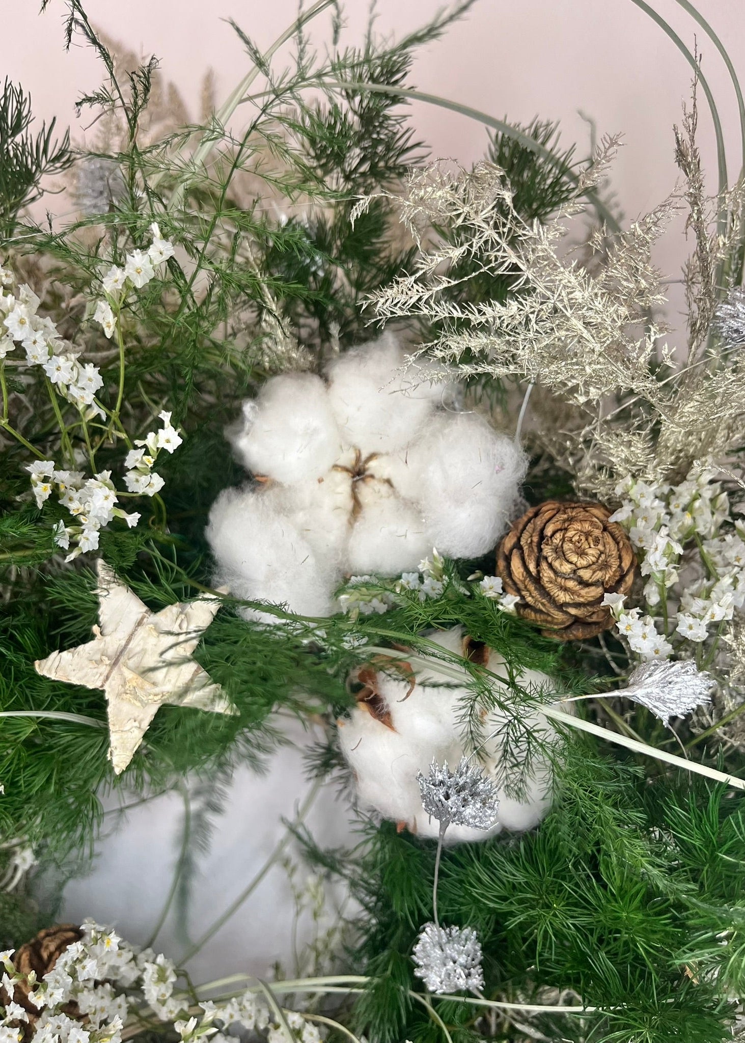 Decorative arrangement with cotton, pinecones, and greenery on a neutral background