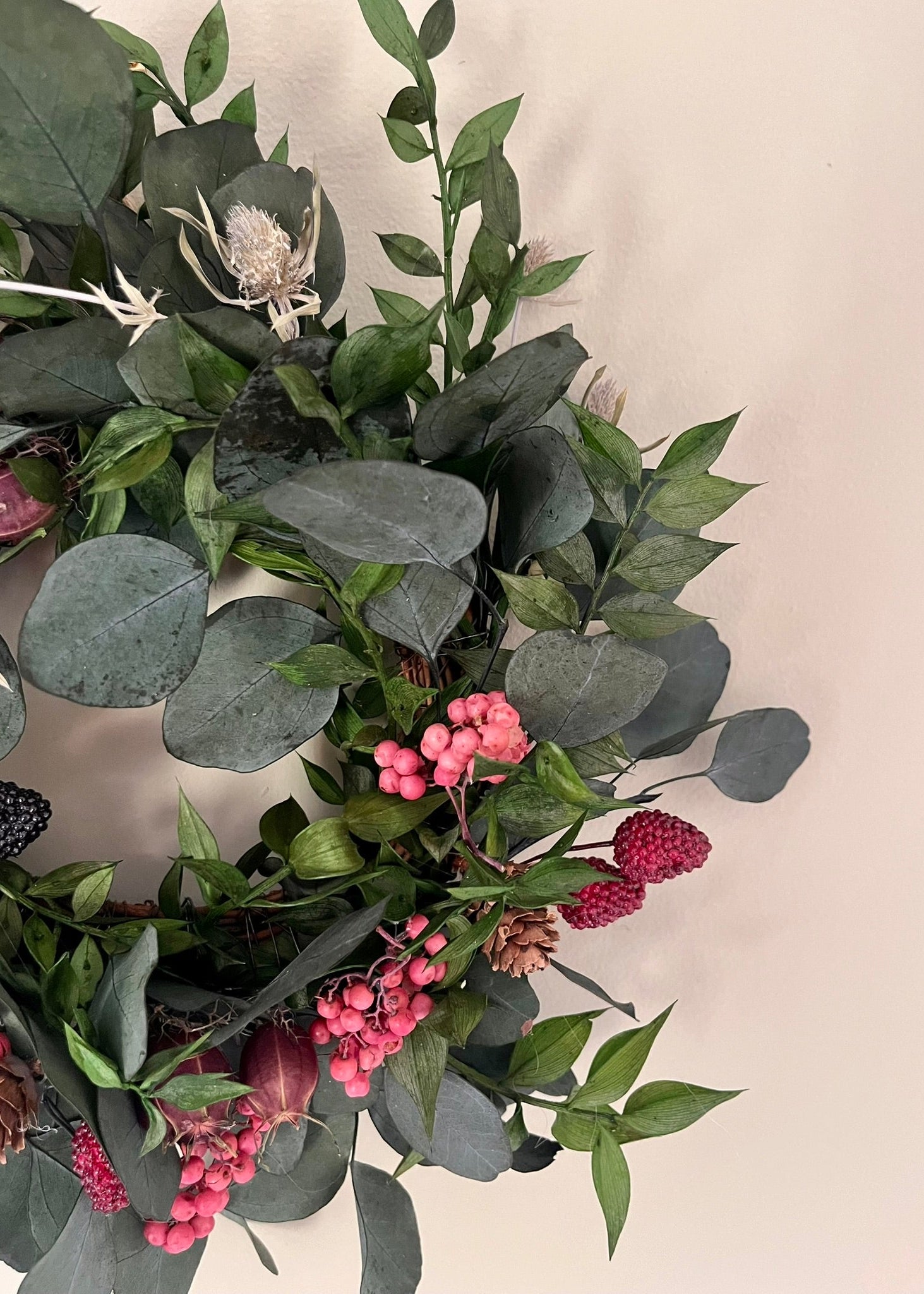Decorative wreath with green leaves and pink berries on a neutral background