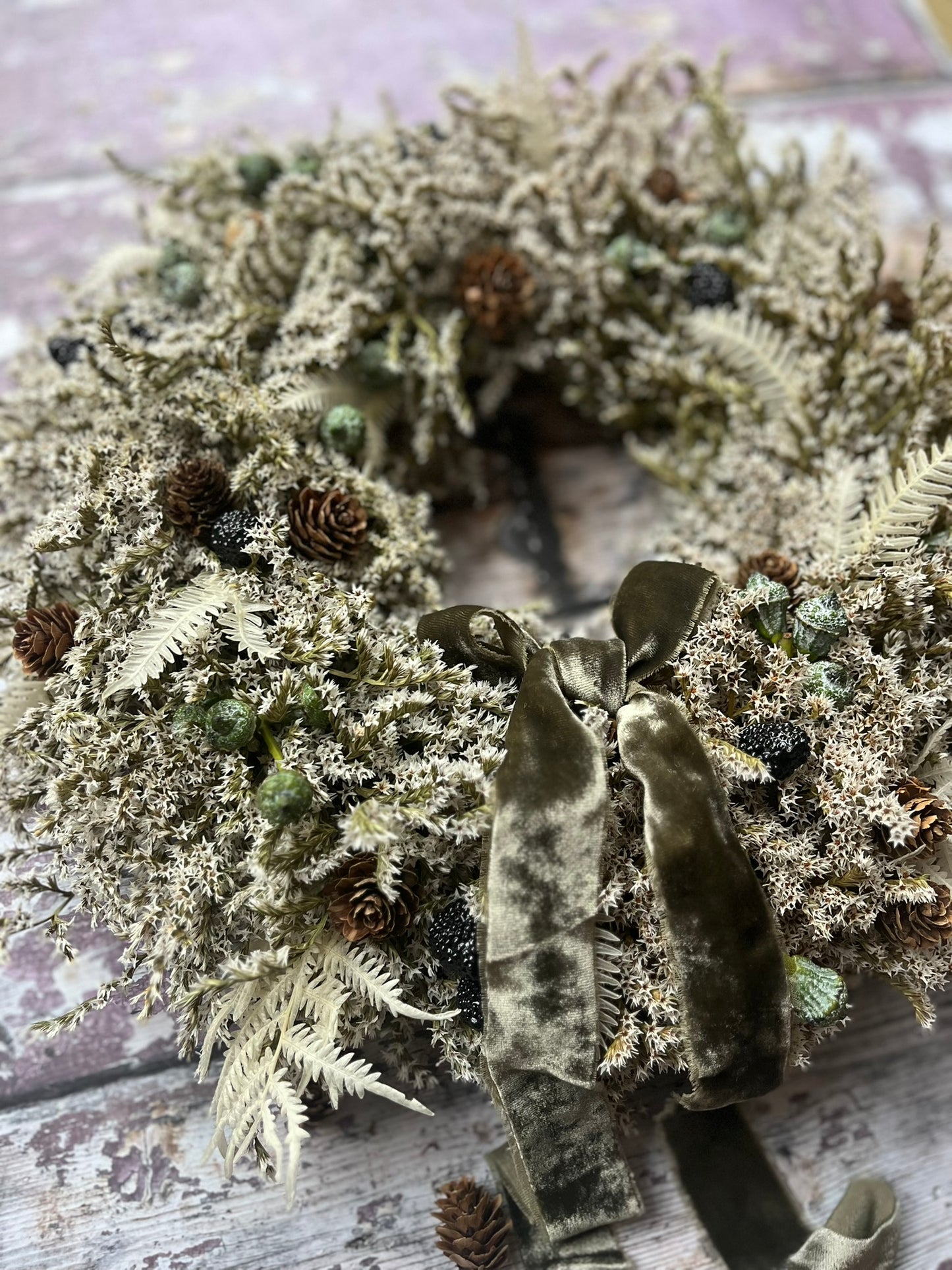 Decorative wreath with greenery and pinecones on a wooden surface
