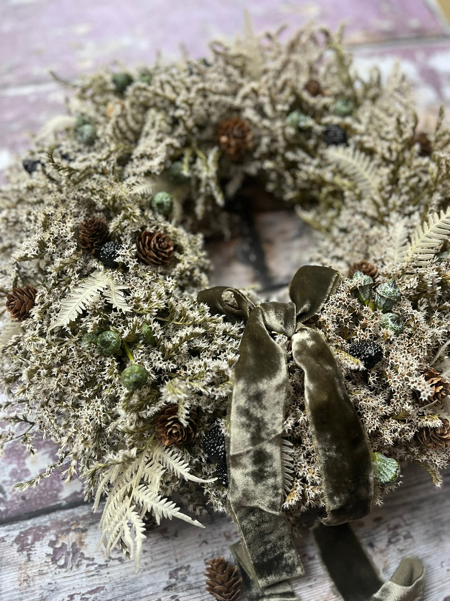 Decorative wreath with greenery and pinecones on a wooden surface