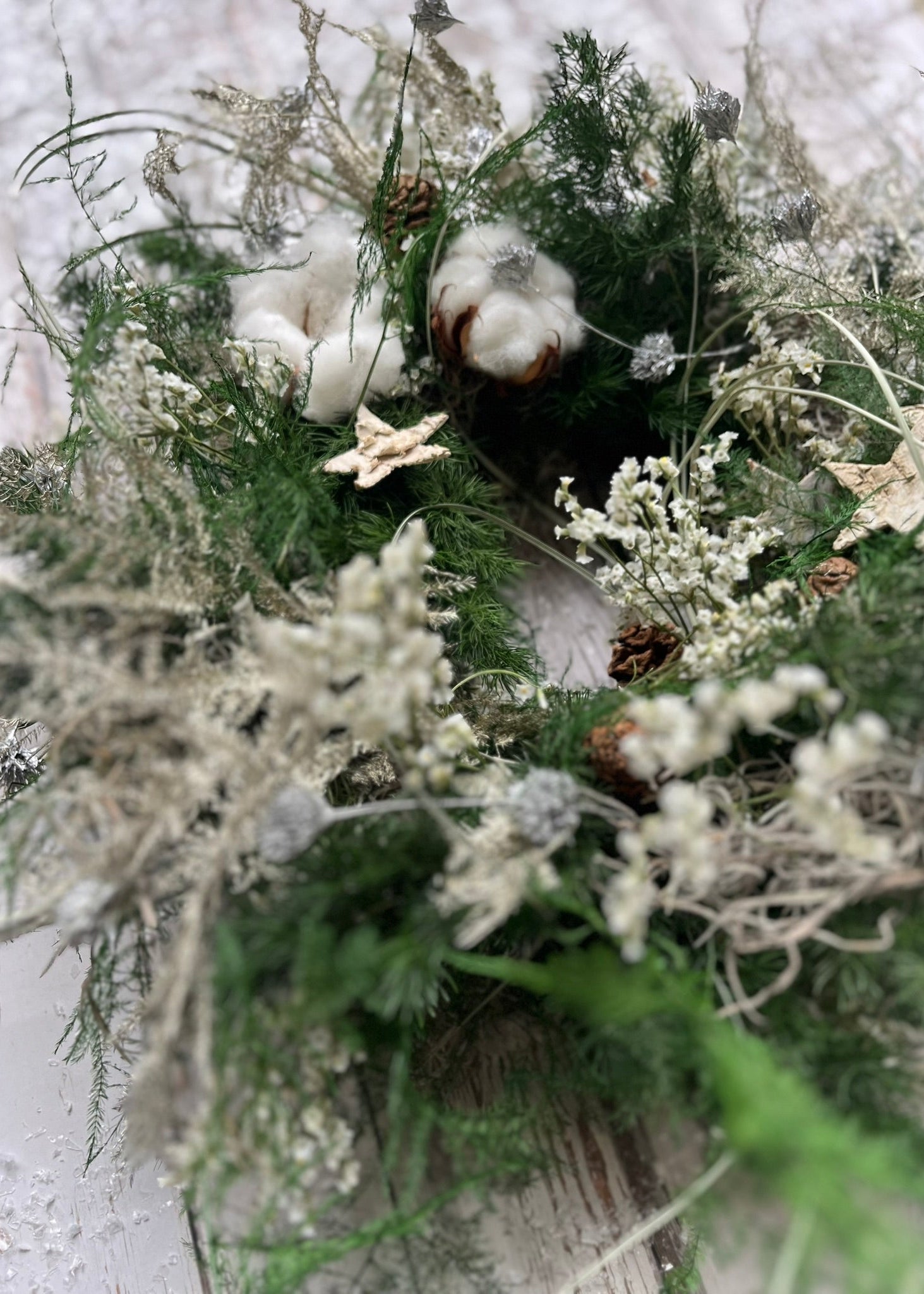 Decorative wreath with greenery, cotton, and pinecones on a light background