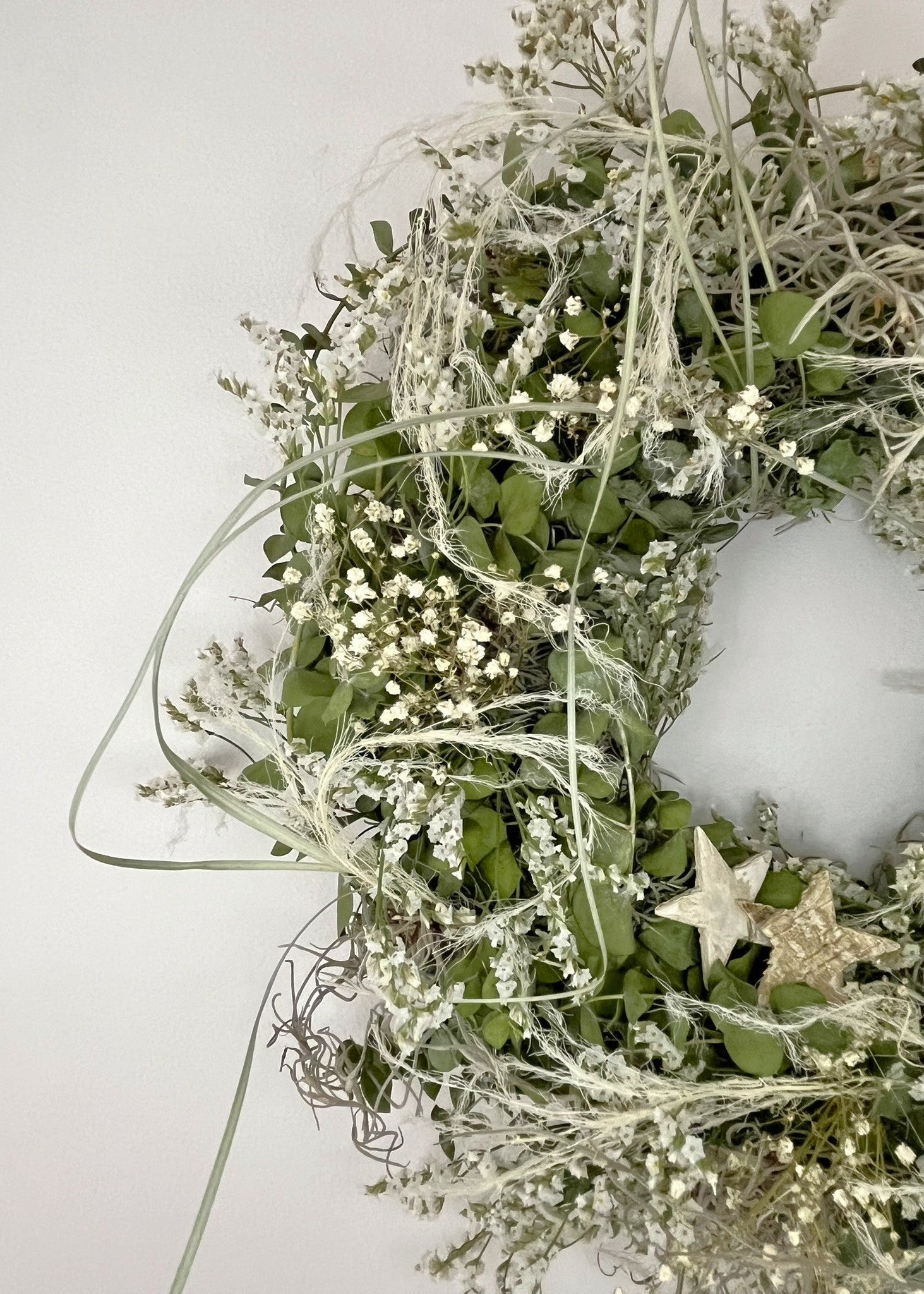 Decorative wreath with greenery and small white flowers on a light background