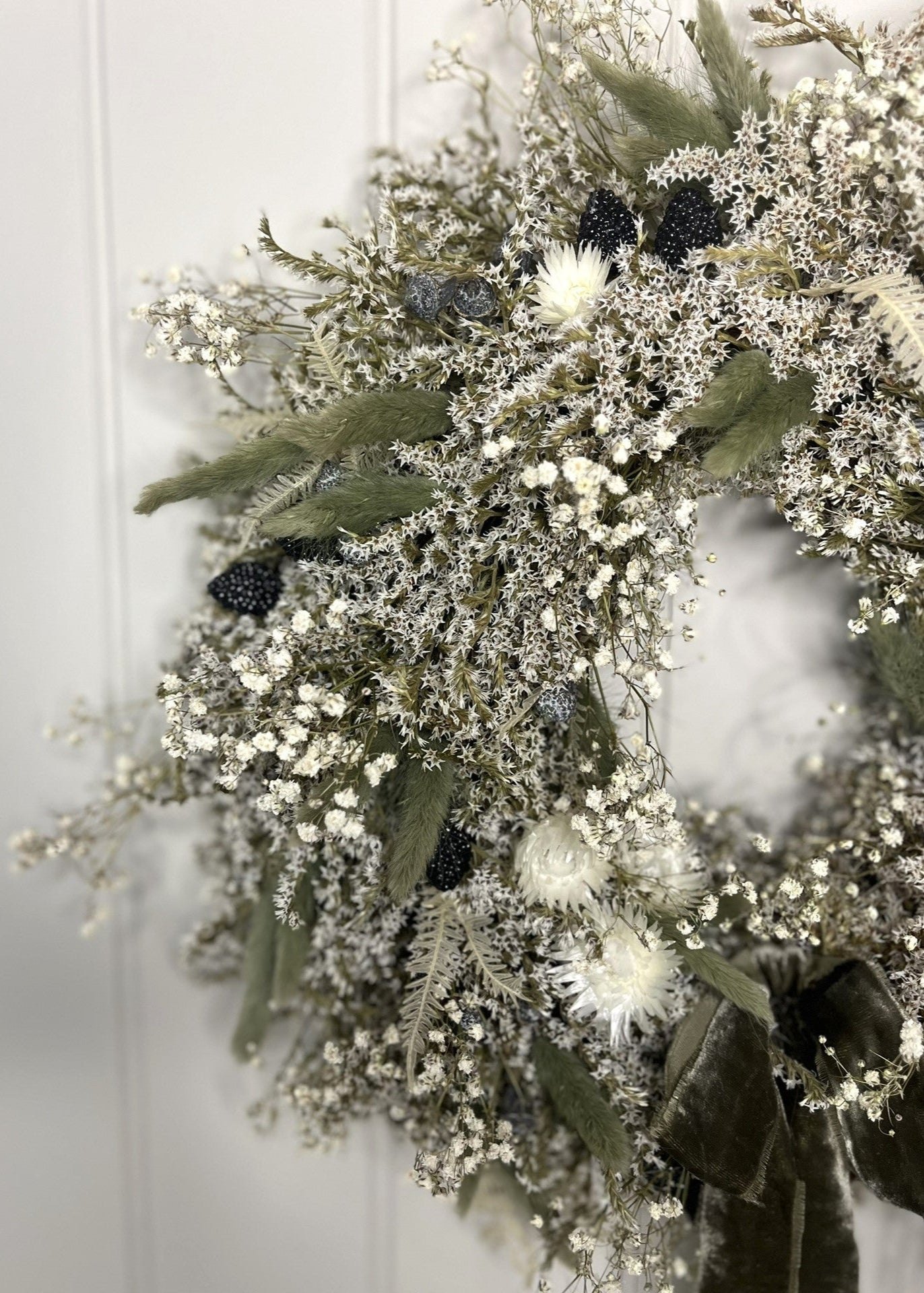 Decorative wreath with greenery, white flowers, and black berries on a white background